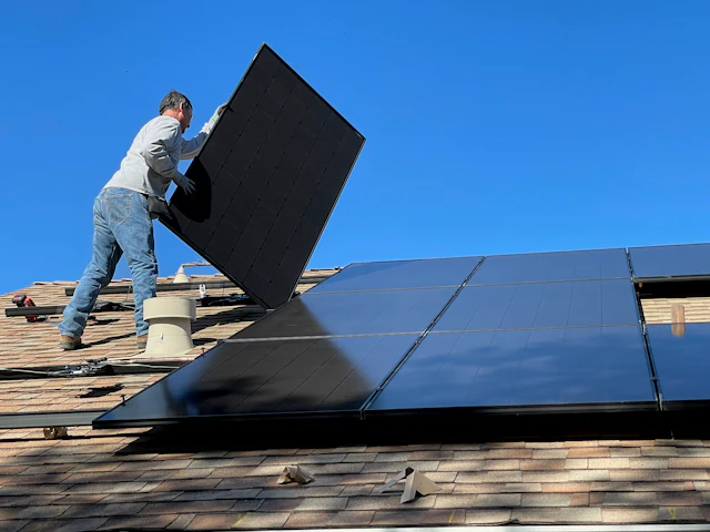 Instalador colocando painel solar preto em um telhado de telhas